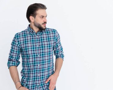Ekose gömlekli genç adam ceplerinde el ele tutuşuyor ve gri arka planda yer almaya çalışıyor. 