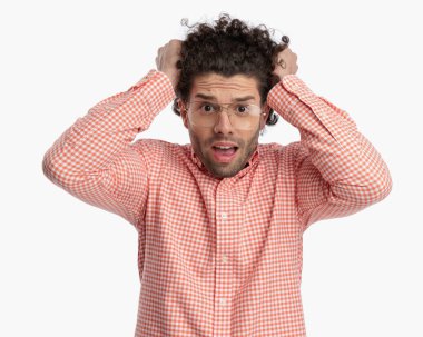 Gözlüklü sinirli genç adam kıvırcık saçlarını çekerken çığlık atıyor ve beyaz arka planda kızgın oluyor.