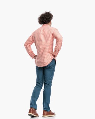 Stüdyoda beyaz arka planda yürürken kalçalarının üstünde el ele tutuşup gözlerini kaçıran sıradan bir genç.