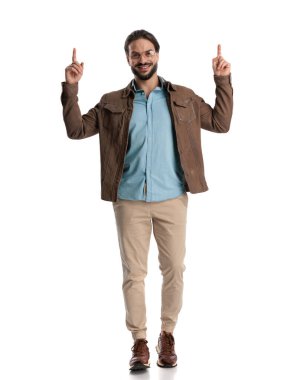 Yakışıklı, gözlüklü, parmağını kaldırıp gülümseyen, yürüyen ve beyaz arka planda poz veren bir adam.