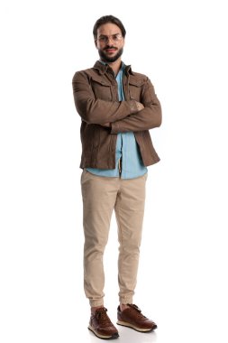 Mutlu sakallı, gözlüklü, gülümseyen ve kollarını kavuşturan beyaz arka planda durup poz veren adam. 