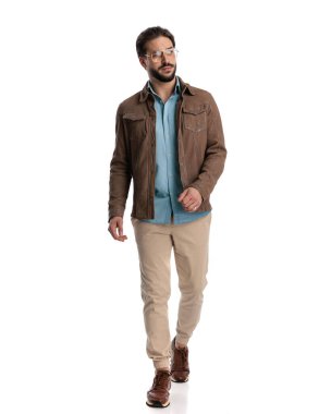 Gözlüklü çekici bir adam. Stüdyoda beyaz arka planda yürüyor.