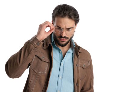 Seksi moda adamı beyaz arkaplan önünde poz verirken aşağı bakıyor ve gözlükleri ayarlıyor 