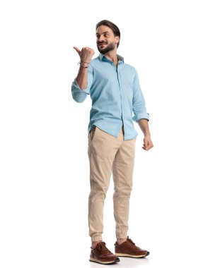 Kot gömlekli sıradan bir genç. Arkasına bakıyor ve beyaz arka planda parmağını omzunun üstünden işaret ediyor. 