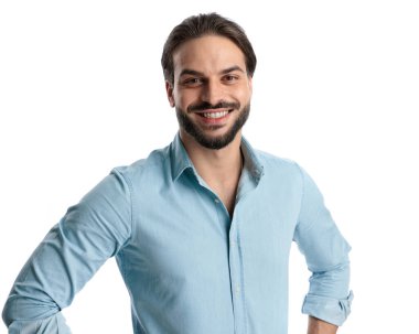 Sakallı, kot gömlekli, gülümseyen ve beyaz arka planda poz veren mutlu genç bir adamın portresi. 