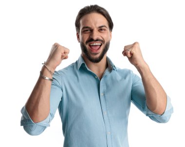 Heyecanlı, sakallı, yumruklarını katlayan ve zaferi beyaz arka planda kutlayan genç bir adam. 