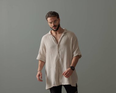 Kendine güvenen, gözlüklü, gri arka planda poz veren havalı bir adam.