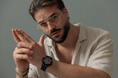 Avuç içlerini bir arada tutan ve gri arka planda ileriye bakan sıradan genç bir adam. 