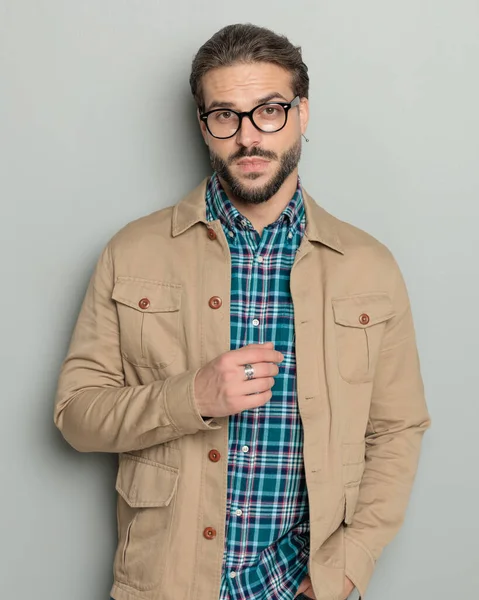 ポケットに手を握り 灰色の背景の前にポーズするベージュジャケットのセクシーなひげ付きカジュアルな男 — ストック写真