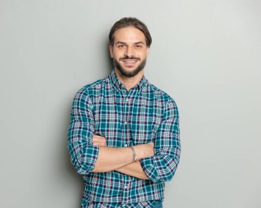 Ekose gömlekli, kollarını kavuşturup gri arka planda gülümseyen gururlu bir adamın portresi. 