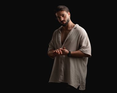 Siyah arka planda avuçlara dokunurken ileri bakan sakallı sıradan bir adam.