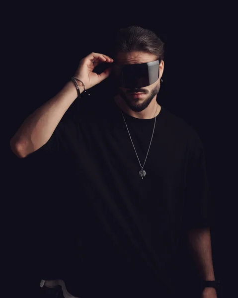 handsome young man in black t-shirt arranging cool fashion sunglasses in front of black background
