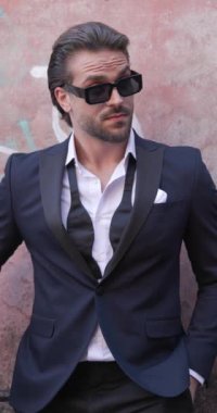 Çekici sakallı adam ceplerinde el ele tutuşuyor, güneş gözlüğü takıyor, kollarını kavuşturuyor ve Romanya 'nın ortaçağdan kalma bir kasabasında gülümsüyor.