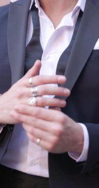 Yakası açık şık bir adamın yüzükleri düzeltirken, takım elbisesini ve gözlüklerini dışarıda tamir ederken görüntülerini kapatın.