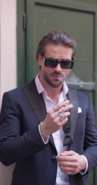 Bağlı olmayan papyonlu ve güneş gözlüklü seksi, zarif bir adam. Eski bir ortaçağ şehrinde sigara içerken yan tarafa bakıyor.