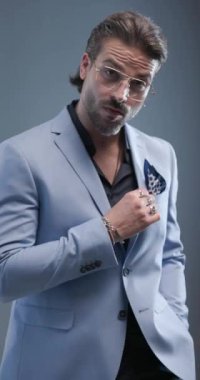 Gözlüklü, el ele tutuşan, el ele tutuşan, avuçlarını ovuşturan, takım elbise tamir eden, çenesine dokunup düşünen, gri arka planda yürüyüp giden seksi genç adam.