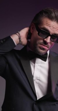 Çekici ve zarif bir adam başının arkasında el ele tutuşuyor, smokin bakıyor ve ayarlıyor, renkli arka planda dönüp gidiyor.