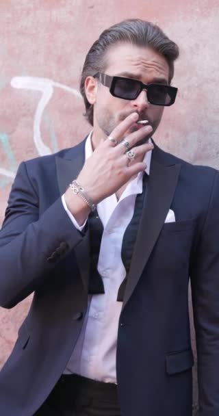 穿着西服的优雅的年轻商人 戴着太阳镜 一边看一边抽烟 一边在户外调整手镯 — 图库视频影像