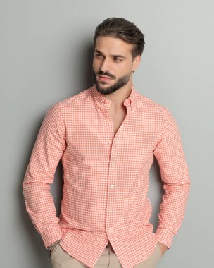 Sakallı, el ele tutuşan ve gri arka planda güven içinde poz veren seksi genç adam.