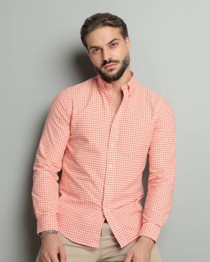 Sakallı yakışıklı genç adam gri arka planda poz veriyor.