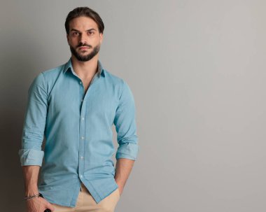 Yakışıklı genç adam el ele duruyor ve gri arka planda ileriye bakıyor.