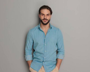 Sakallı, el ele tutuşan ve gri arka planda ileriye bakan genç bir gazcı. 