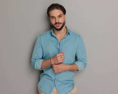 Kot tişörtlü seksi sakallı adam elele tutuşuyor ve gri arka planda ileriye bakıyor. 