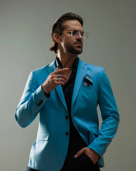 stock image handsome bearded man with glasses holding hand in pocket and looking to side while posing in front of grey background