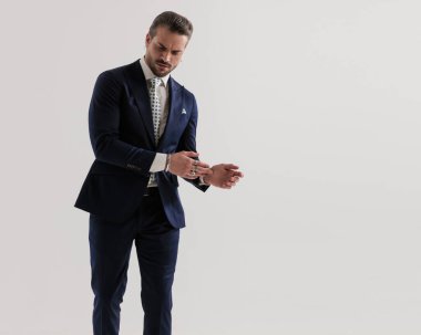 Lacivert takımlı yakışıklı, zarif bir adamın portresi. Gri arkaplan önünde yere bakıyor ve ellere dokunuyor. 