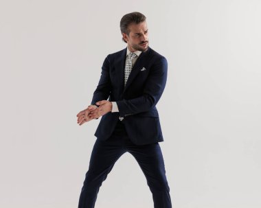 Avuçlarını ovuşturan ve gri arka planda havalı poz veren üst sınıf bir iş adamı. 