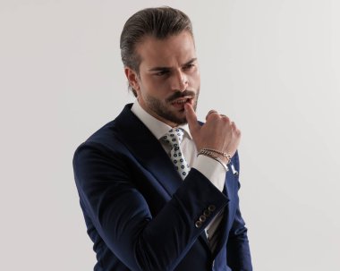 Şehvetli, zarif iş adamının portresi. Gri arka planda dudaklara dokunurken gözlerini kaçırıyor.