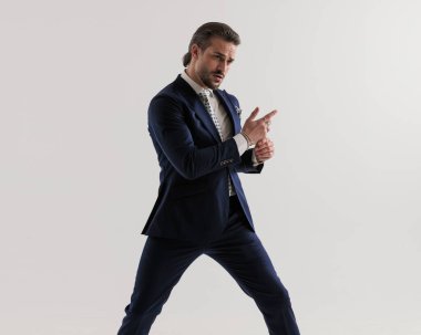 Lacivert takım elbiseli çekici bir gencin portresi. Gri arka planda serin bir şekilde kollarını tutuyor. 