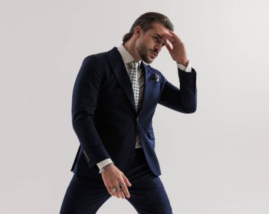 Düşünceli genç adam el ele tutuşuyor ve gri arka planda zarif lacivert bir takım elbise ve mendil giyerek yüzünü çeviriyor.