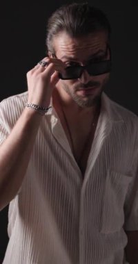 Tıraşsız seksi genç adam güneş gözlüğünü ayarlıyor, kendine güveniyor ve polis ışıkları açıkken gri arkaplanın önüne bakıyor.