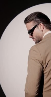 Zarif genç adam dönüyor, yana bakıyor, çene dokunuyor ve gri arka planda yuvarlak spot ışığı önünde düşünüyor