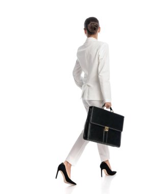 Beyaz takım elbiseli zarif bir kadın beyaz arka planda yürürken ve beyaz arka planda yan yan bakmak isterken. 