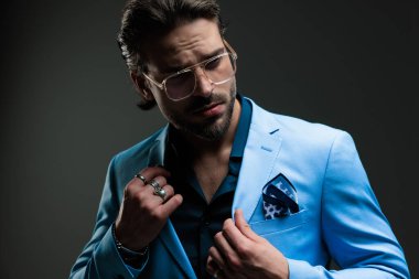 Gözlüklü, kendine güvenen zarif iş adamının portresi mavi takımı ayarlıyor ve koyu gri arka plana bakıyor.