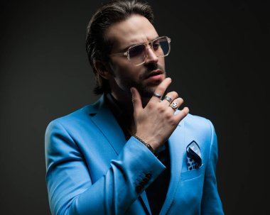 Düşünceli, zarif iş adamının portresi. Gözlüklü, çenesine dokunan ve koyu gri arka planda düşünen.