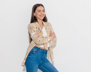 Mutlu iş kadını desenli ceketiyle kollarını kavuşturup gri arka planda gülümsüyor.