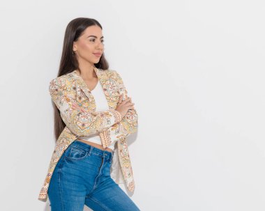 Eşarp desenli ceketli kendine güvenen bir iş kadını kollarını kavuşturup gri arka planın önüne geçmeye çalışıyor. 