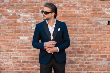 Transilvanya 'nın ortaçağdan kalma bir şehrinde taş duvarların önünde el ele tutuşan, güneş gözlüklü, tıraşsız zarif bir adamın portresi.