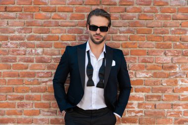 Orta çağdan kalma bir şehirde, el ele tutuşup kayaların önünde poz veren, güneş gözlüklü, kendinden emin üst sınıf bir işadamının portresi.