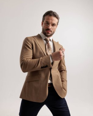 Gri arka planda el kol hareketi yaparken ve ileriye bakarken el ele tutuşup gözlük takan yakışıklı genç iş adamı.