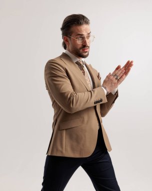 Gözlüklü zarif bir iş adamı gri arka planda avuçlarını ovalıyor.