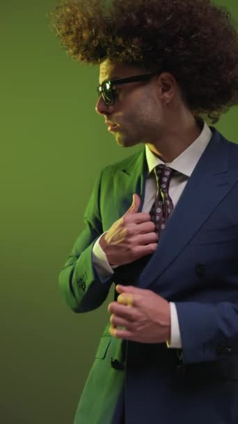 スーツを調整しながら横に探している官能的なエレガントな男性の垂直ビデオ 楽しみにして カラフルな背景の前に沈黙のジェスチャーを作る — ストック動画