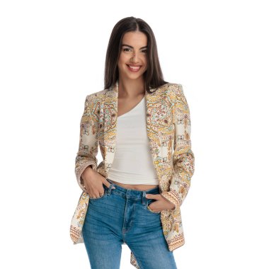 Ceketli, cebinde el ele tutuşan, beyaz arka planda ileriye bakan ve gülümseyen çekici bir kız.