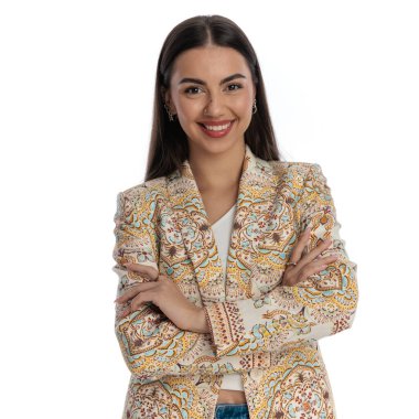 Sıradan moda kadını ileriye bakıyor, gülümsüyor ve beyaz arka planda poz verirken kollarını kavuşturuyor.. 