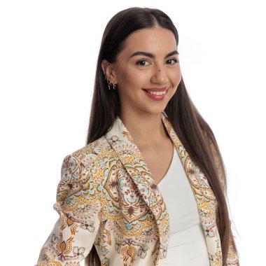 Stüdyoda beyaz arka planda poz verirken ileriye bakıp gülümseyen güzel bir genç kadının portresi.