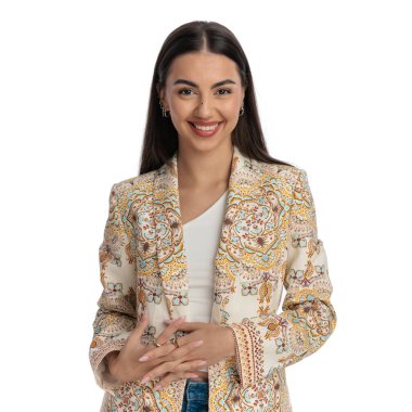 Ceketli çekici bir genç kız el ele tutuşuyor, ileriye bakıyor ve beyaz arka planda gülümsüyor.