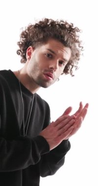 Siyah kapüşonlu, siyah kapüşonlu, avuçlarını ovuşturan ve gri arka planda kendine güvenen yakışıklı sıradan bir adamın dikey videosu.